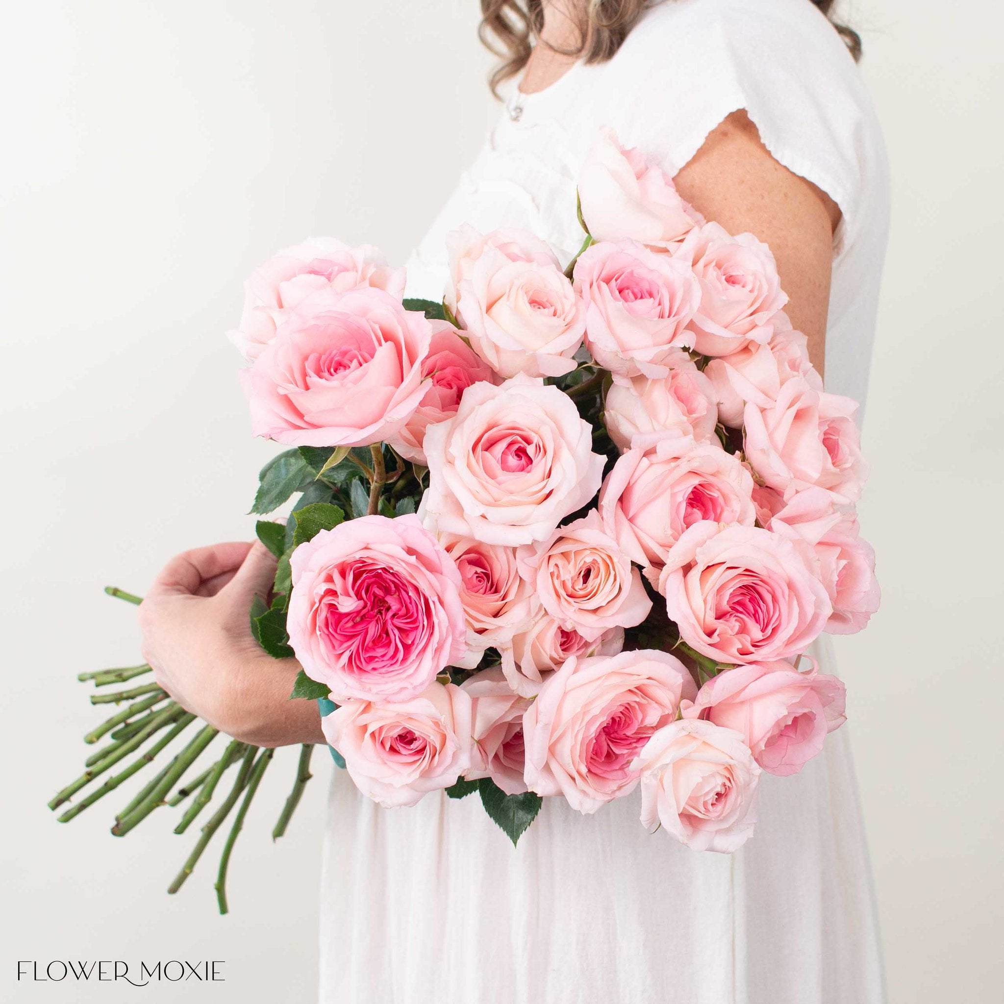 Bouquet of pink roses held by a person wearing a white dress on a light background.