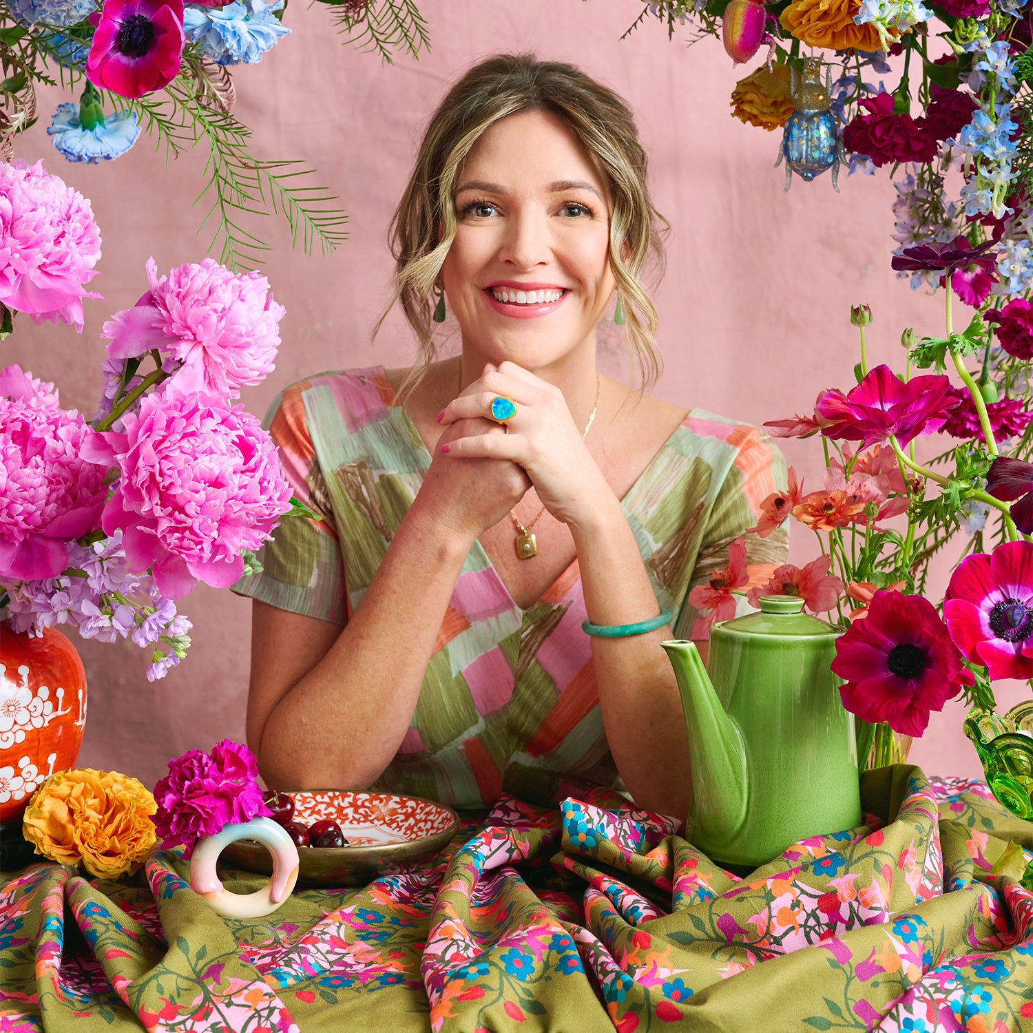Woman sitting at a table with flowers and a green teapot on a colorful background