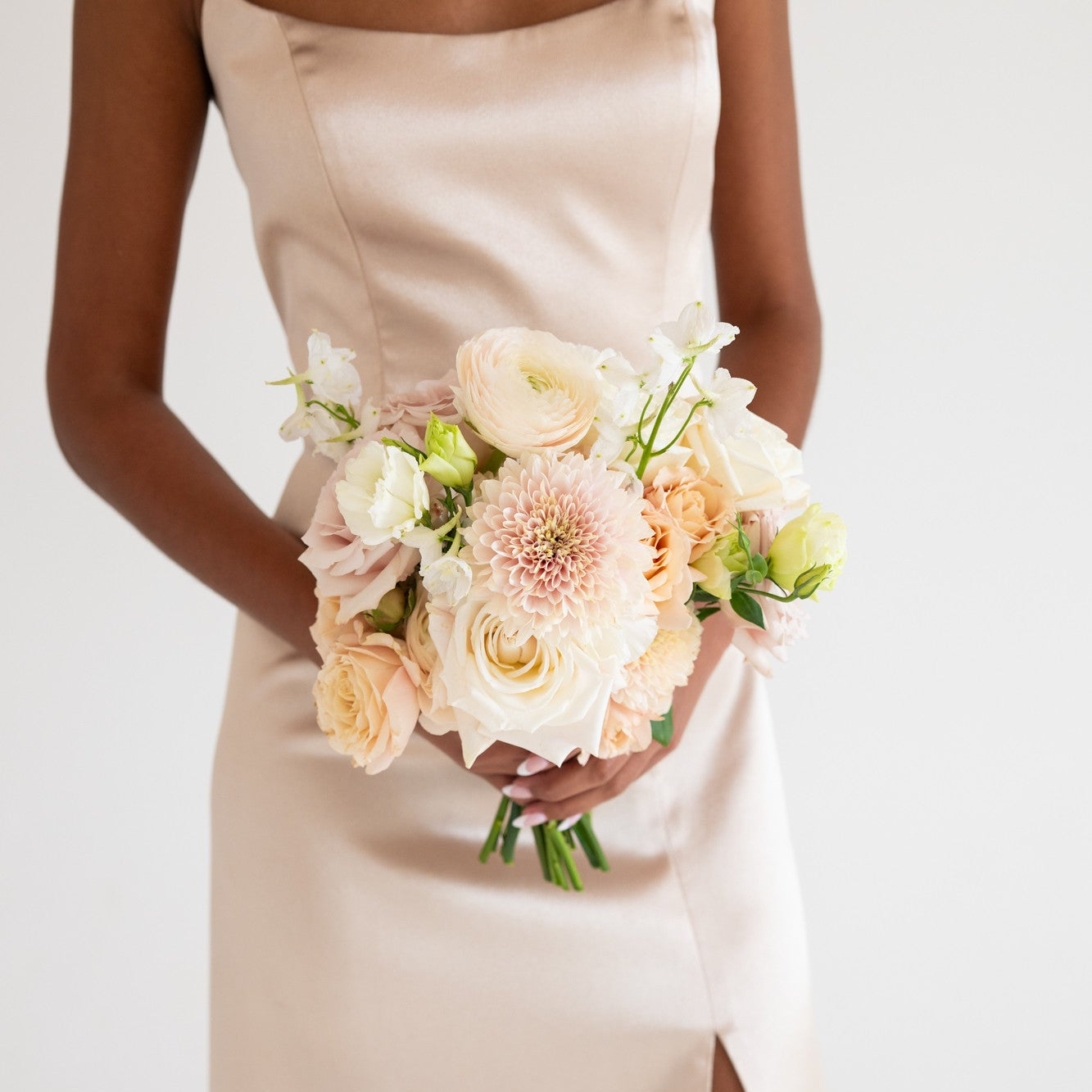 A woman wearing a strapless champagne-colored satin dress with a thigh-high slit, holding a neutral bouquet of flowers.