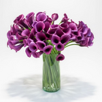 Bouquet of purple calla lilies in a clear vase on a wooden surface.