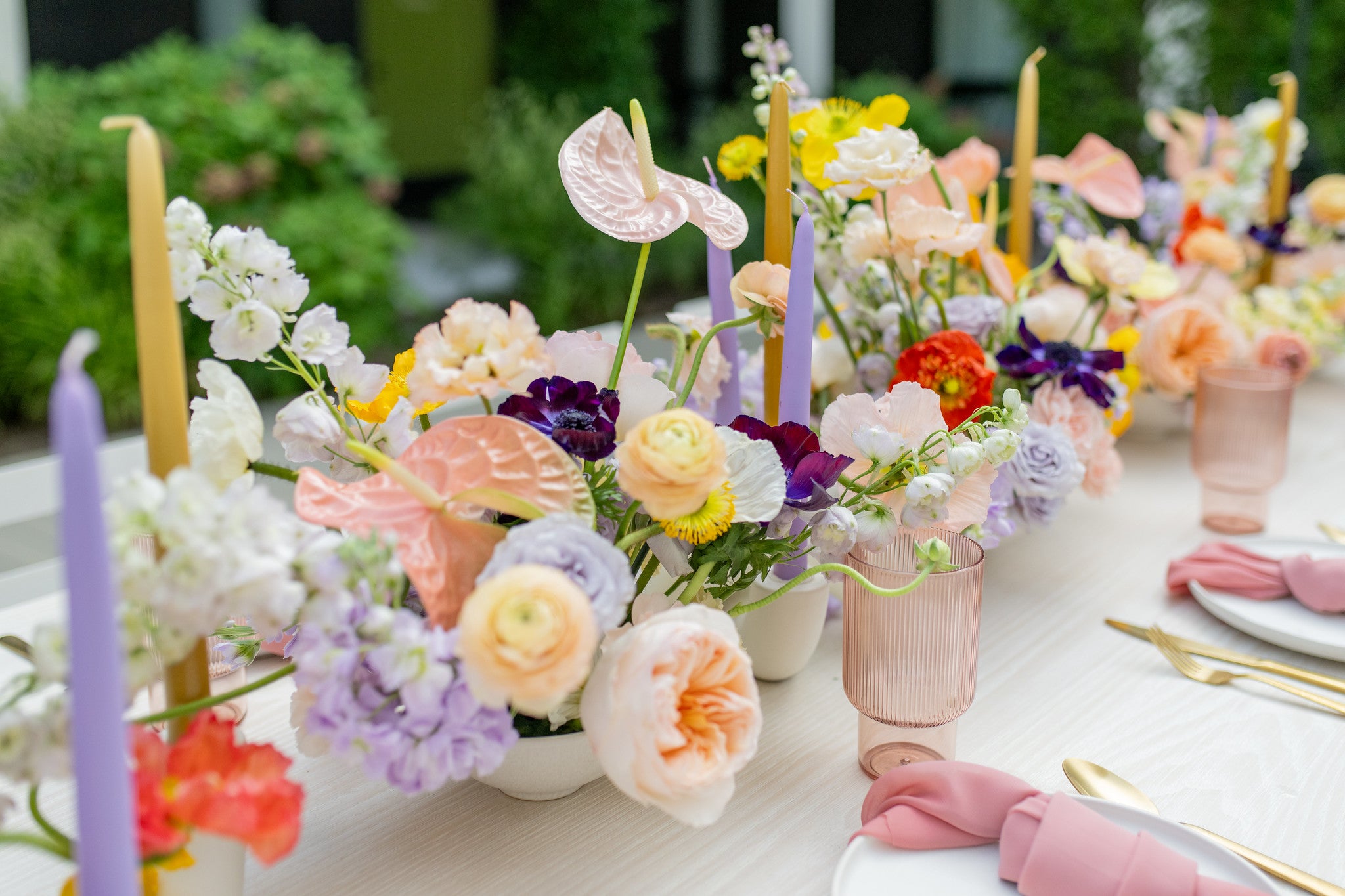 Table decorated with candles and centerpieces with Anthuriums, Delphiniums, Garden Roses, Anemones, Carnations, and Stocks